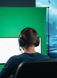 Ein Streamer sitzt vor seinem eingerichteten Greenscreen, auf dem eine Gaming-Szene zu sehen ist.
