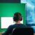 Ein Streamer sitzt vor seinem eingerichteten Greenscreen, auf dem eine Gaming-Szene zu sehen ist.