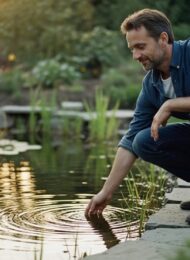 Mann betrachtet zufrieden seinen neu angelegten, naturnahen Gartenteich im Abendlicht.